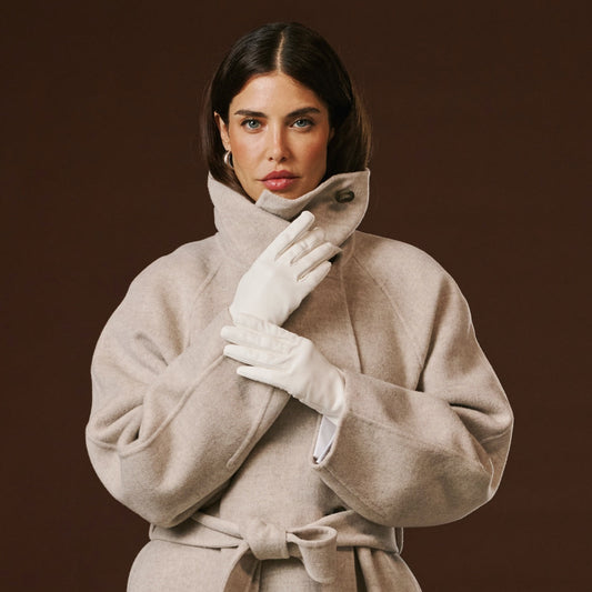 Woman wearing a beige coat and white gloves against a brown background