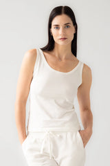 Woman wearing a white sleeveless top and pants against a plain background