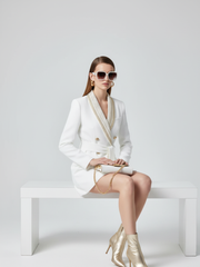 Woman in a white suit sitting on a white bench against a light gray background