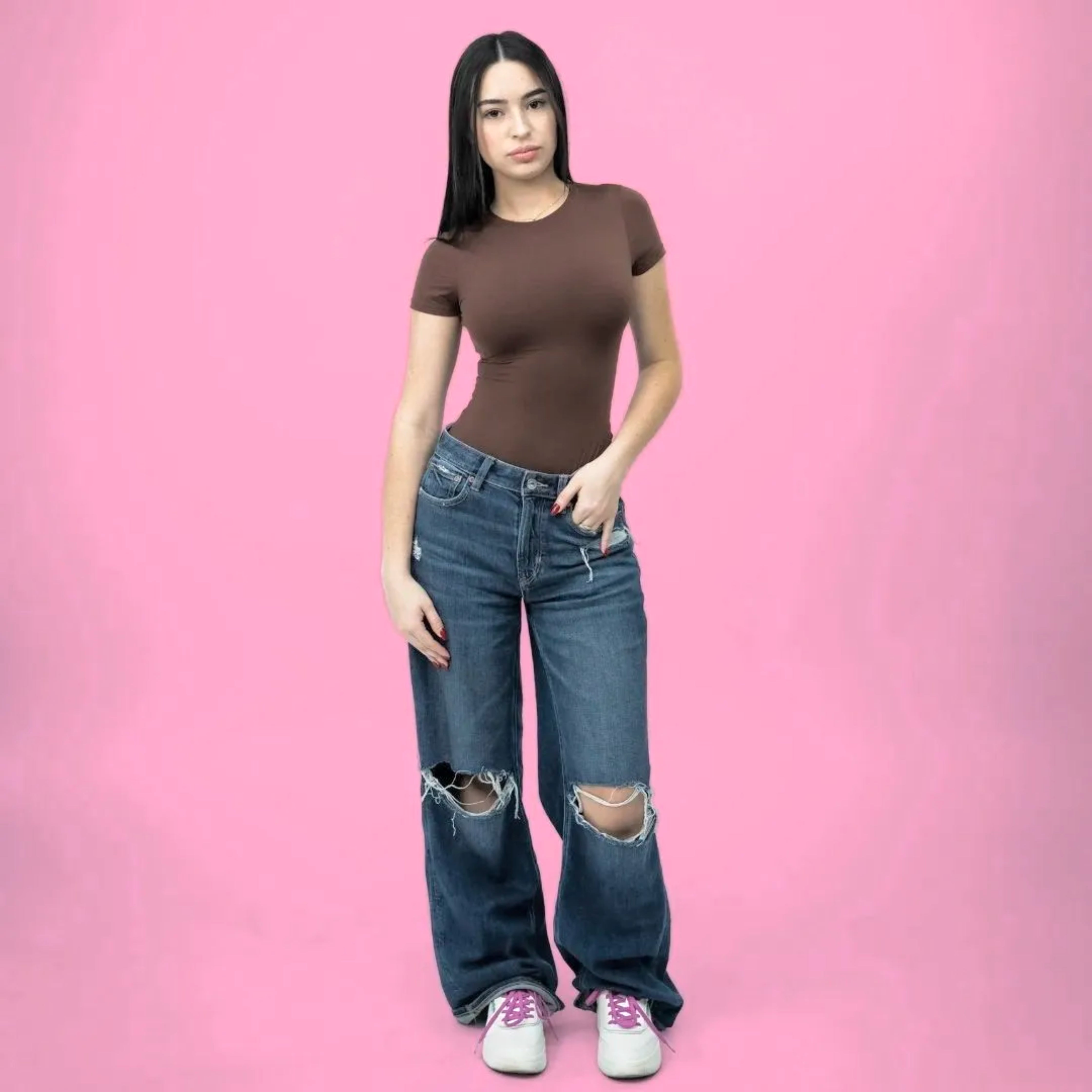 Woman wearing a brown top and blue jeans on a pink background