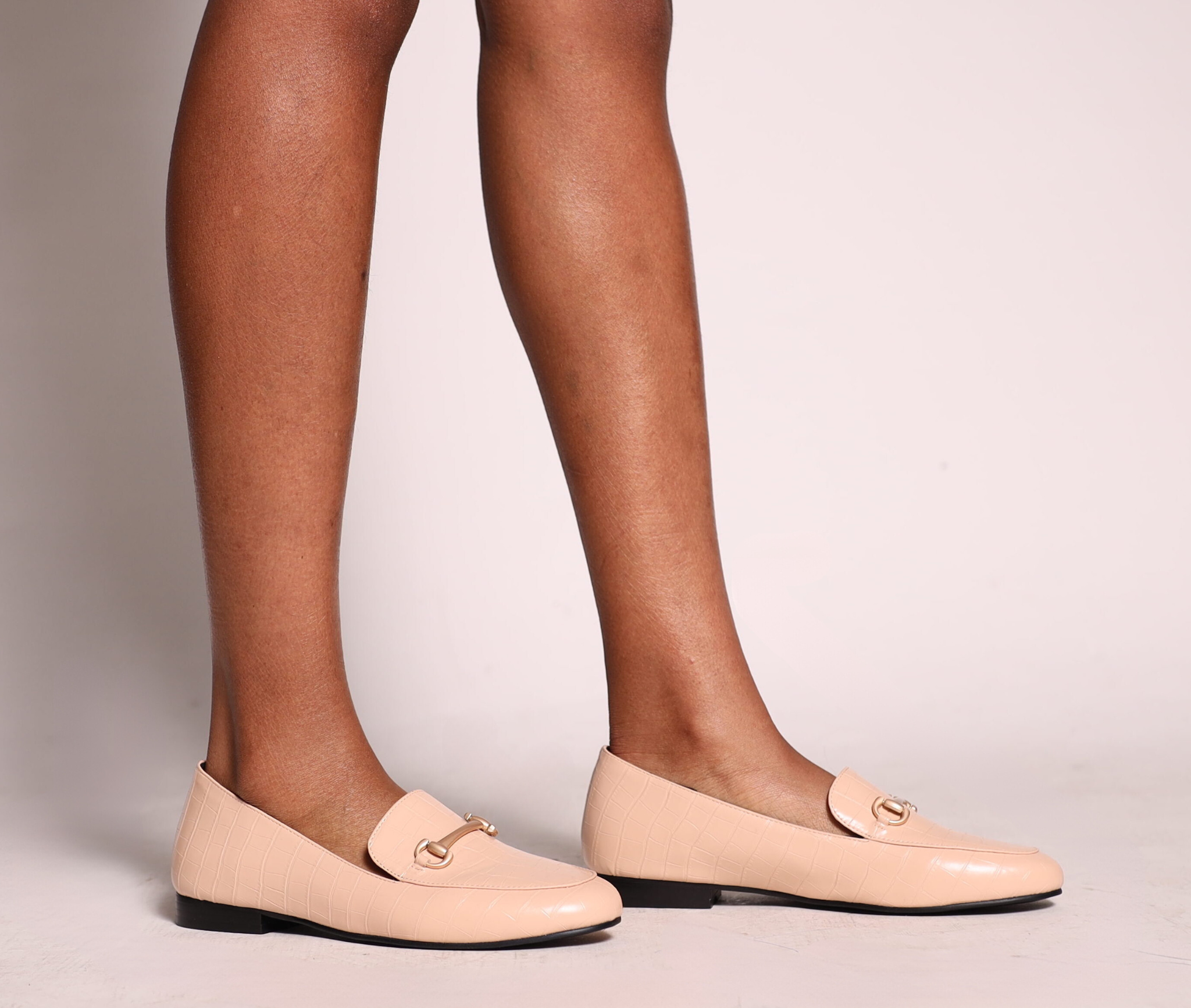 Beige loafers worn with tights on a neutral background