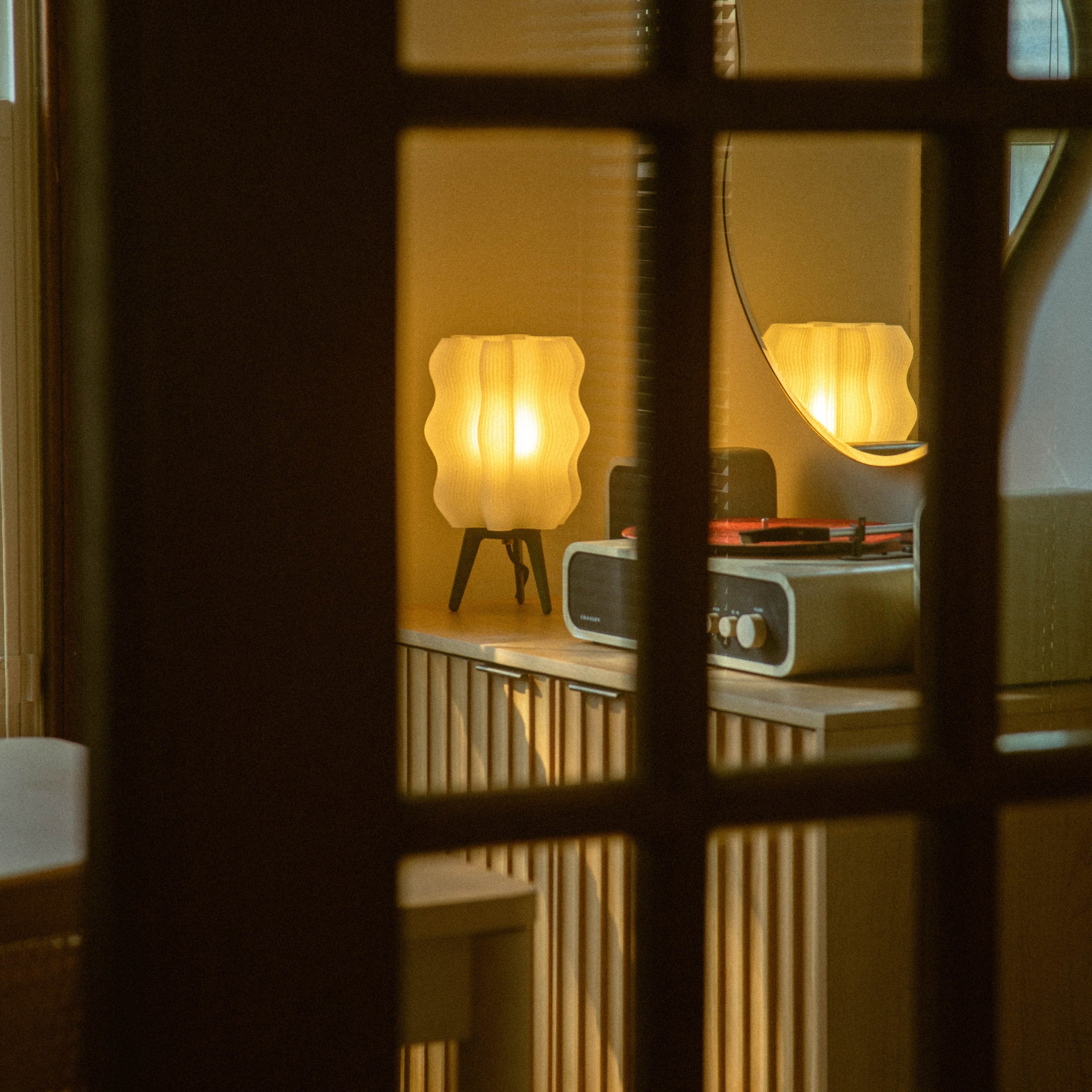 Vintage radio and lamp on a shelf with a warm glow, seen through a window with bars.