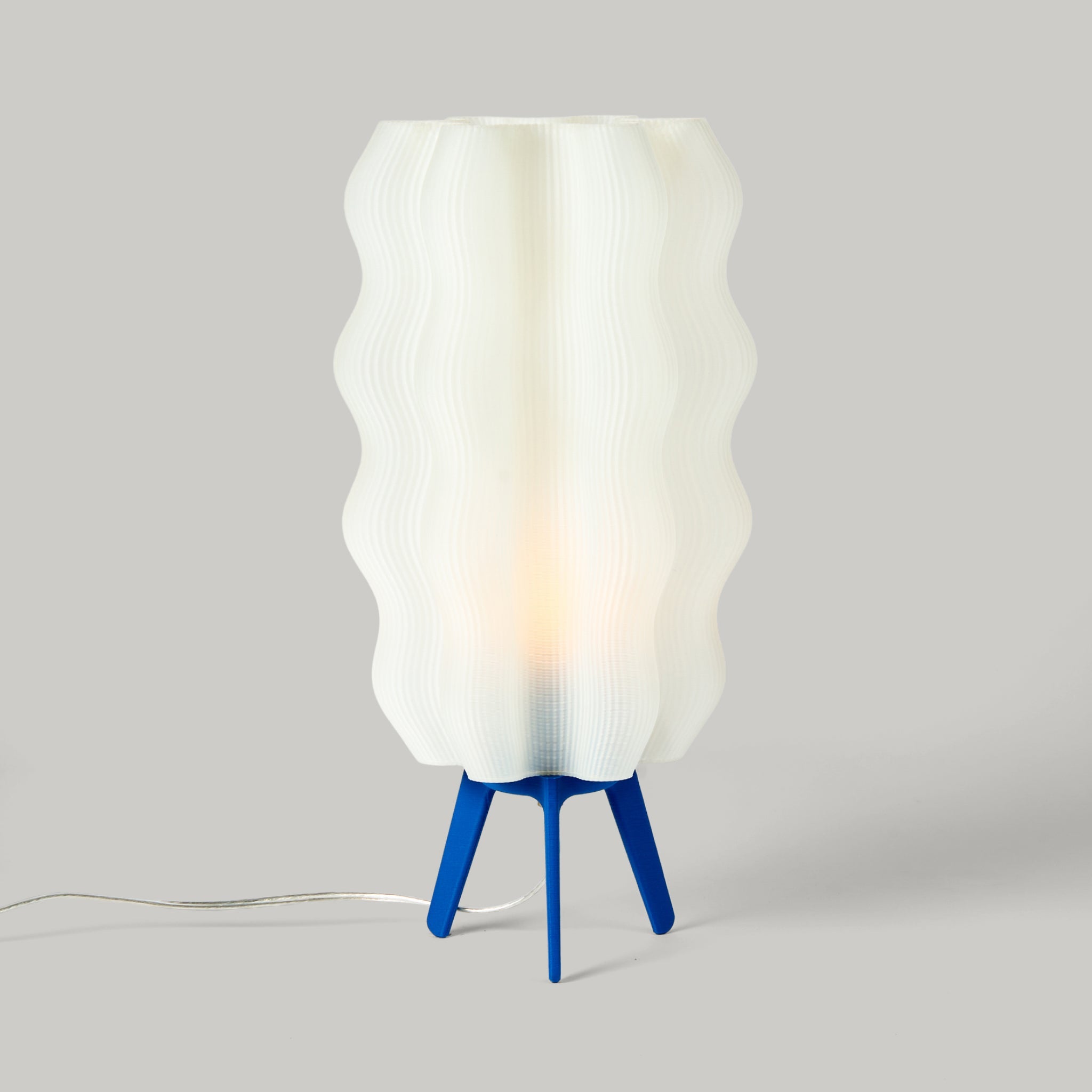 Lamp with a white wavy shade and blue base on a gray background