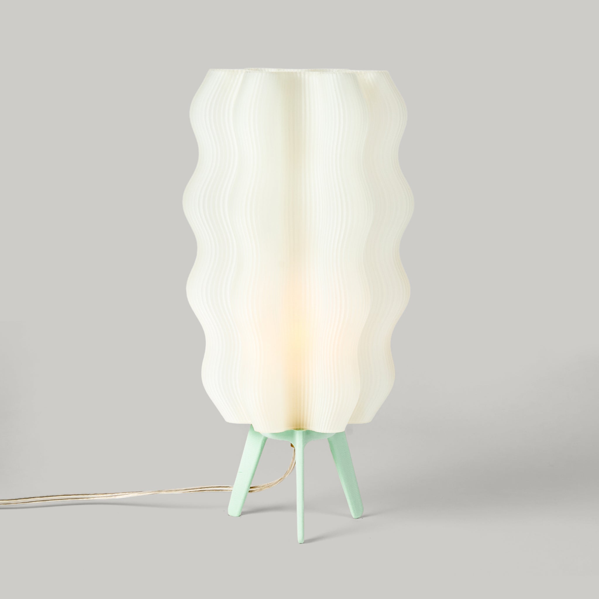 Lamp with a white wavy shade and green base on a gray background