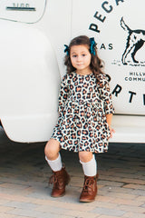 Young girl in a leopard print dress standing in front of a white vehicle with text and graphics.