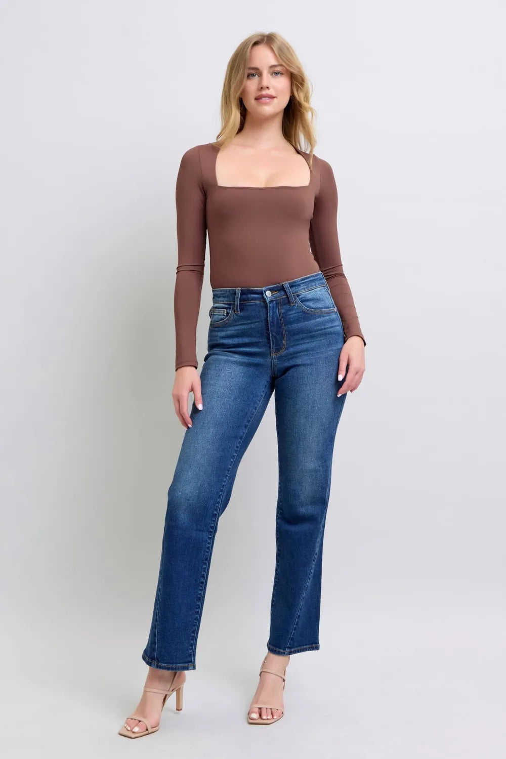 Woman wearing a brown long-sleeve top and blue jeans on a white background