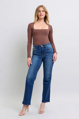 Woman wearing a brown long-sleeve top and blue jeans on a white background