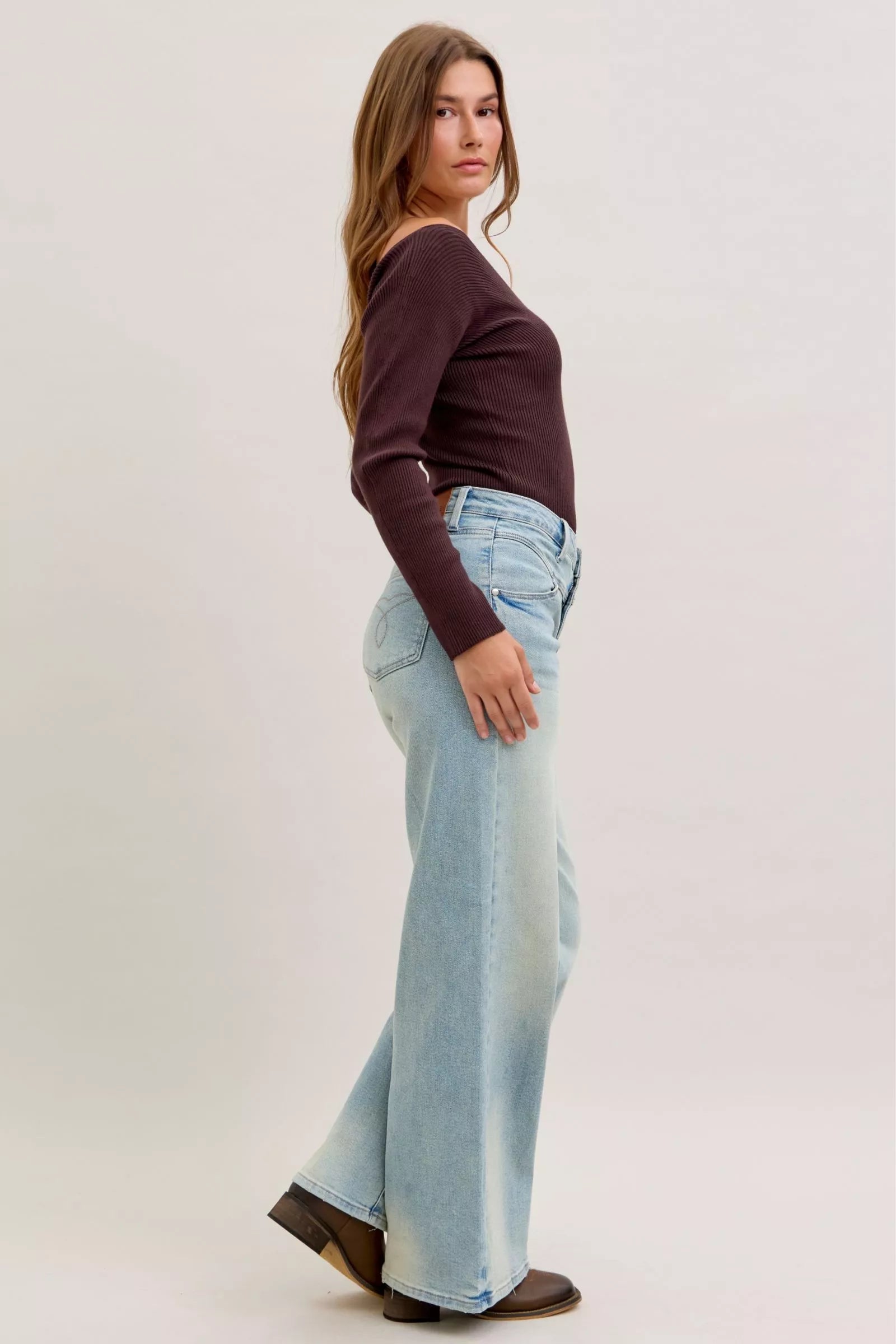 Woman wearing a brown top and light blue jeans on a plain background