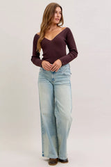 Woman wearing a burgundy long-sleeve top and light blue jeans on a white background