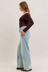 Woman wearing a dark purple sweater and light blue jeans on a plain background