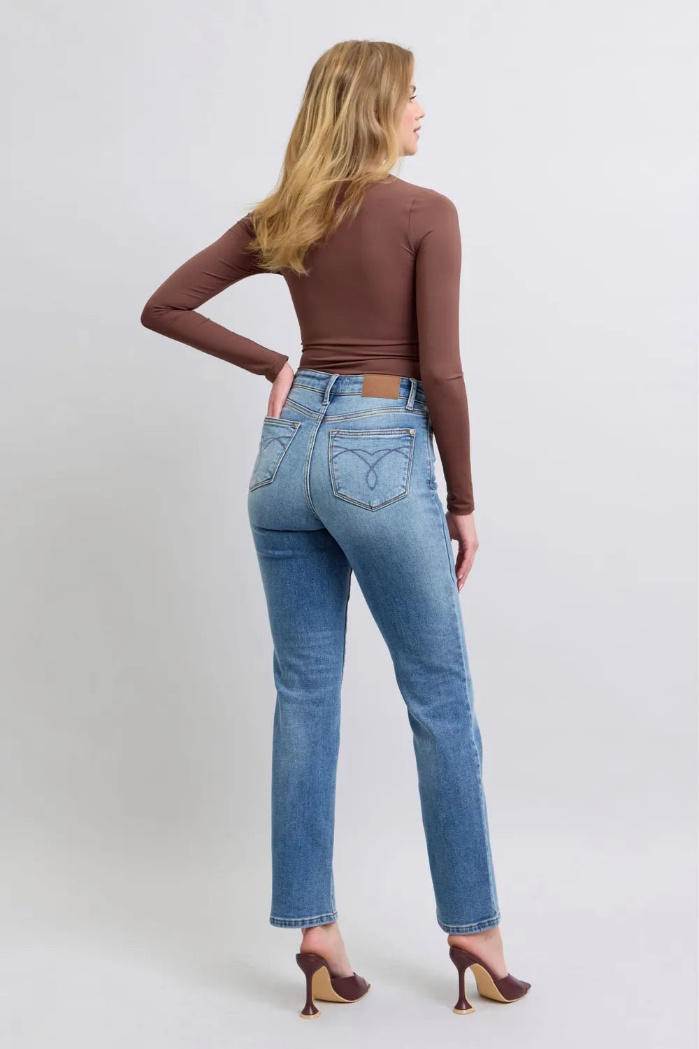 Woman wearing blue jeans and a brown top on a white background