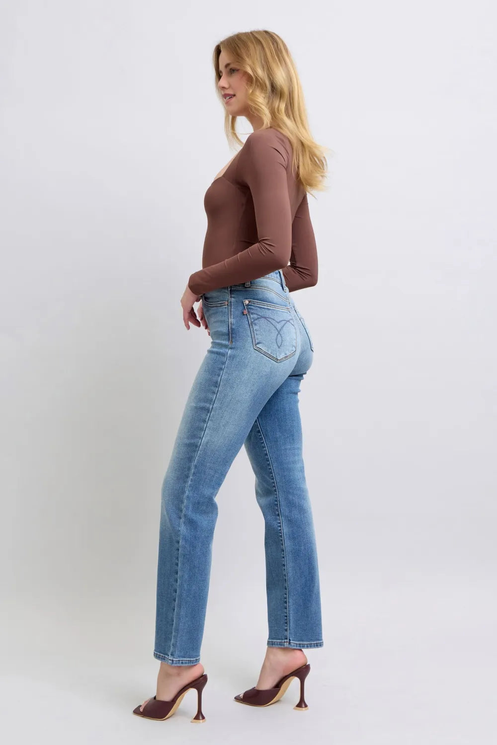 Woman wearing blue jeans and a brown top on a white background