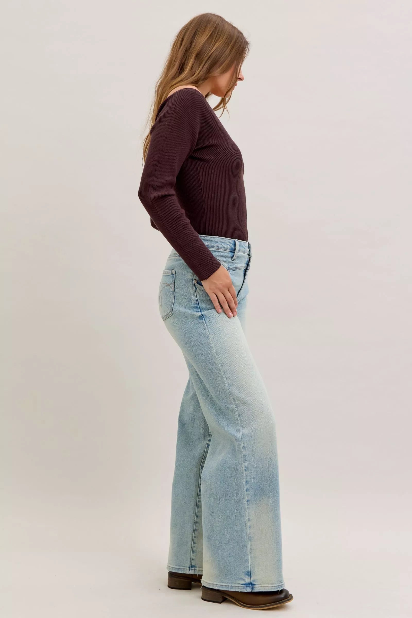 Woman wearing light blue jeans and a dark brown top on a white background