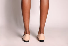 Beige flat shoes worn with tights on a plain background