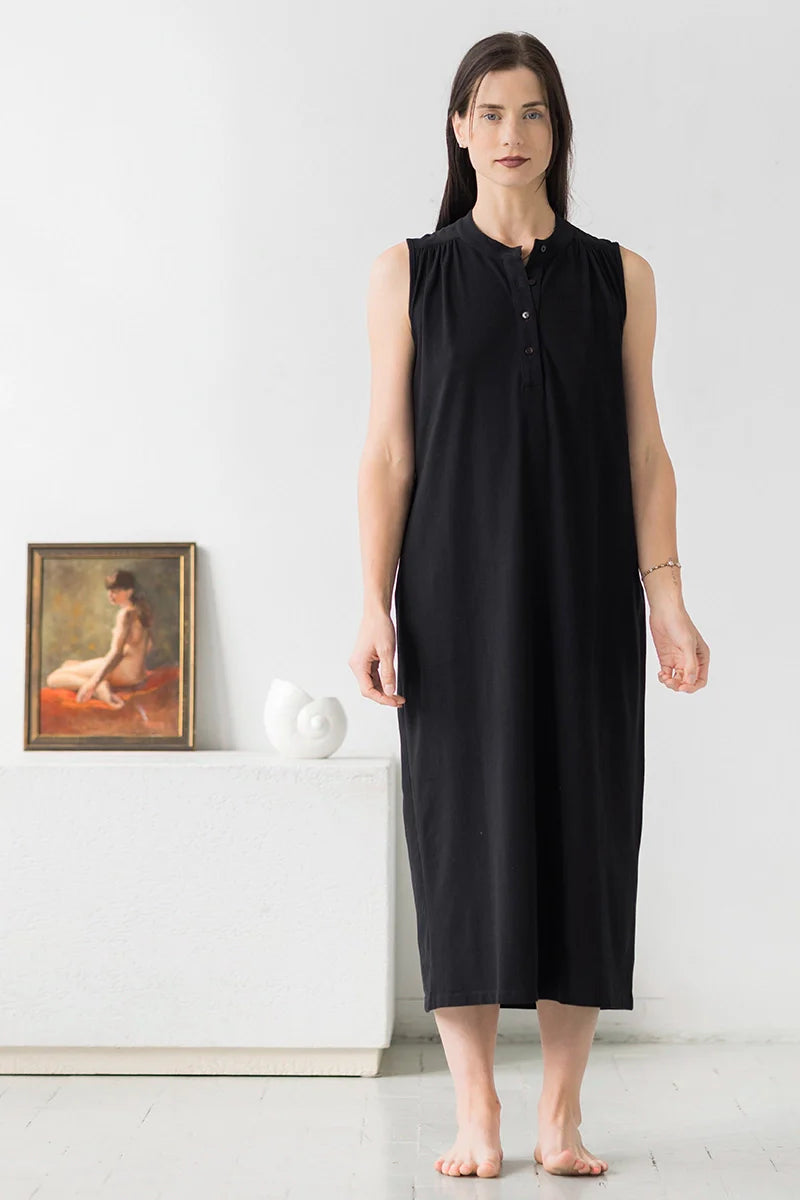 Woman wearing a black sleeveless dress standing in a minimalistic room.