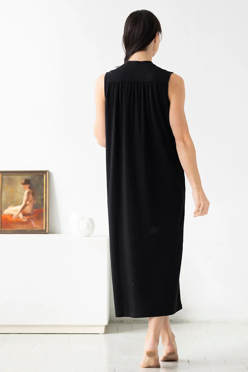 Woman wearing a black sleeveless dress standing in a minimalistic room with a painting on the wall.