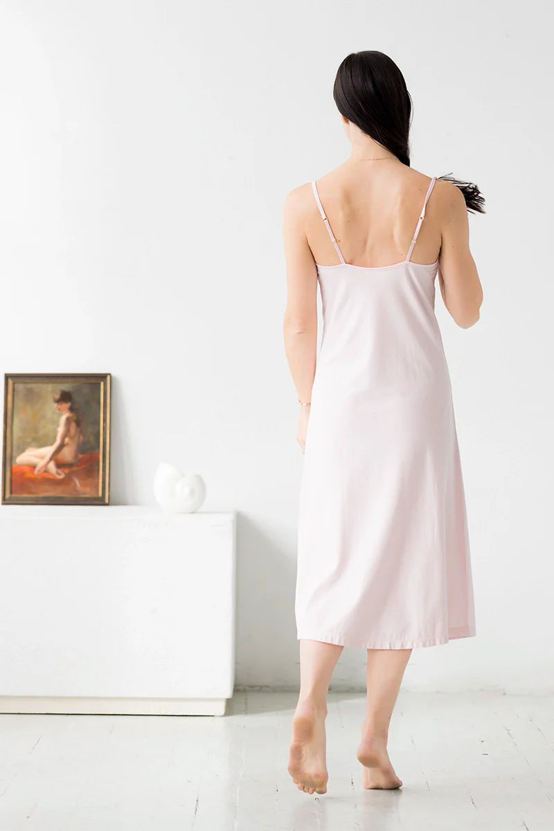 Woman wearing a light pink slip dress in a minimalistic room.