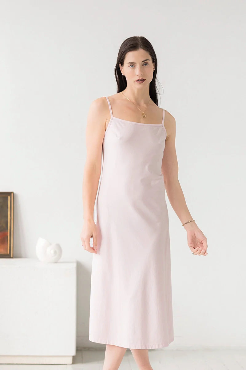 Woman wearing a light pink slip dress against a white background