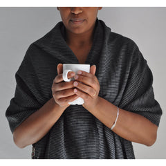 Person wearing a dark gray shawl holding a white mug against a plain background