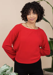 Woman wearing a red sweater standing in front of a beige wall with plants.