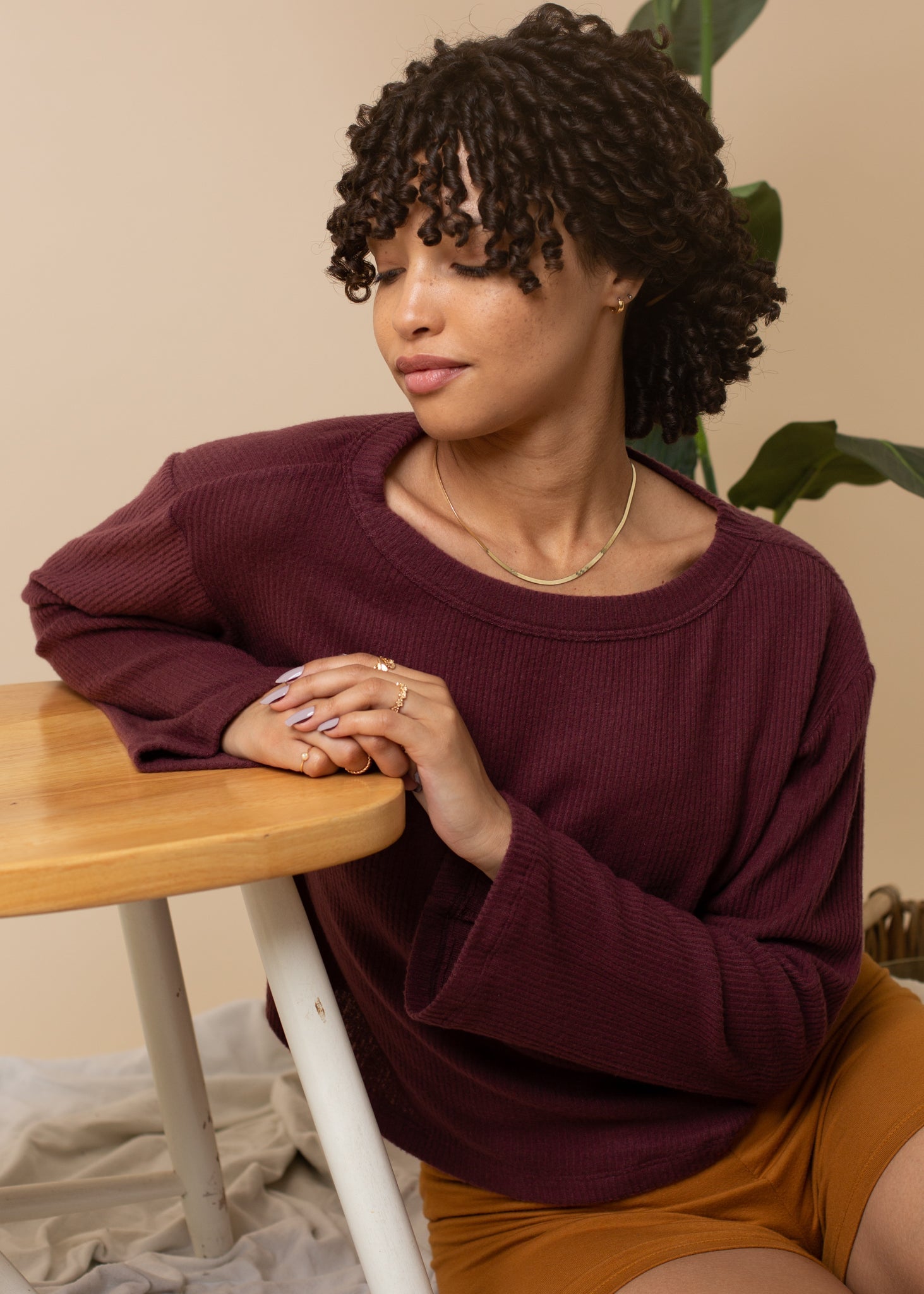 Woman wearing a burgundy sweater sitting at a wooden table with a beige background