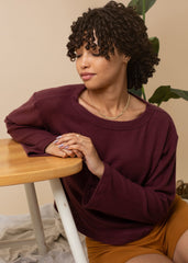 Woman wearing a burgundy sweater sitting at a wooden table with a beige background