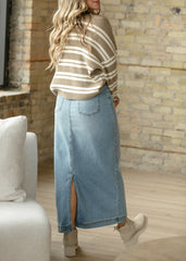 Woman wearing a striped sweater and denim skirt in a room with a stone wall.