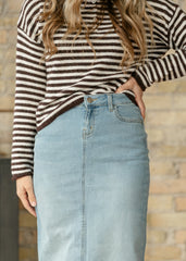 Person wearing a striped sweater and denim skirt against a wooden wall.