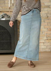 Person wearing a striped shirt and denim skirt standing against a brick wall.