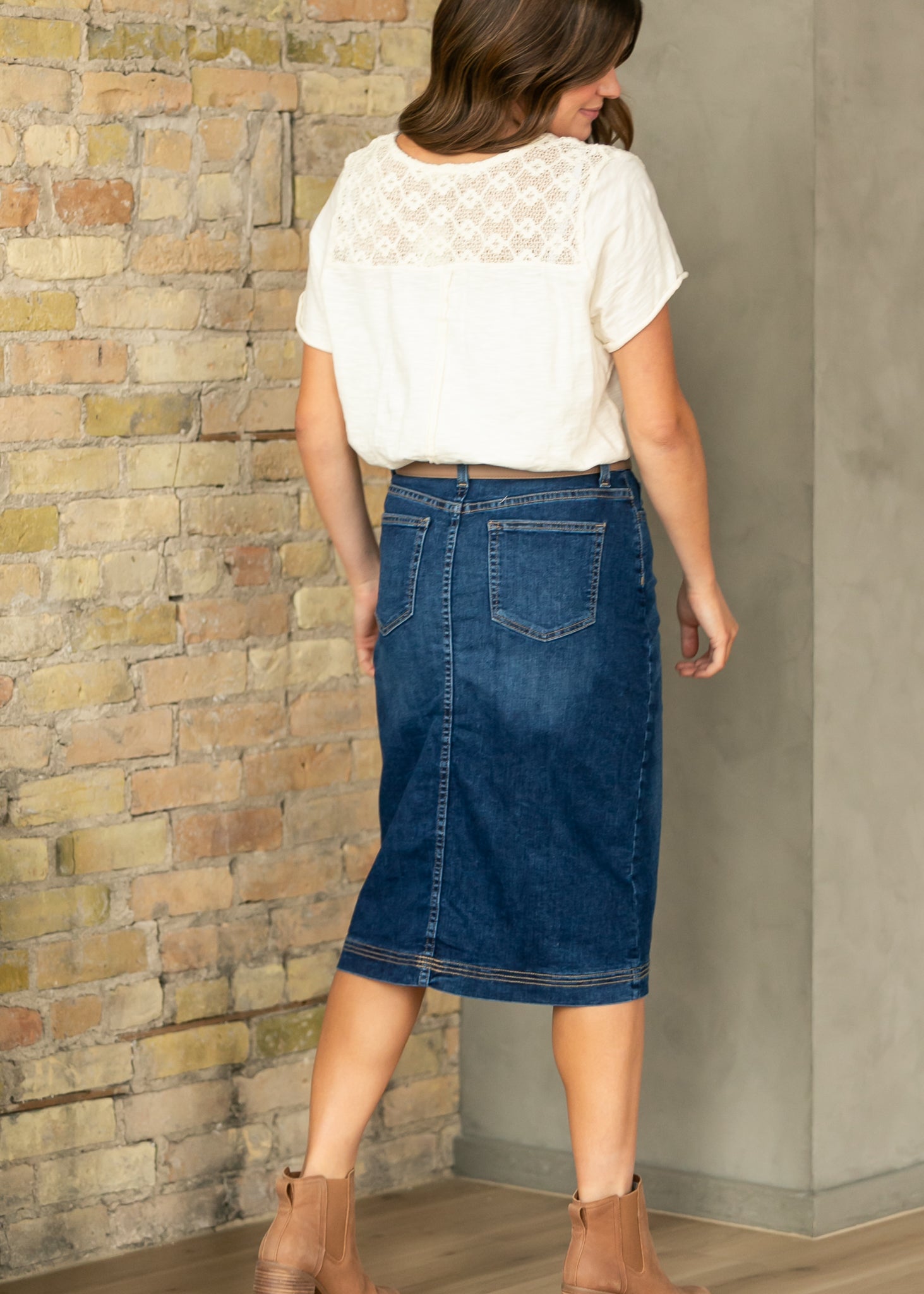 Woman wearing a white top and blue denim skirt against a brick wall.