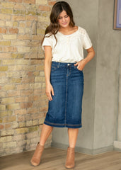 Woman wearing a white blouse and blue denim skirt against a brick wall.
