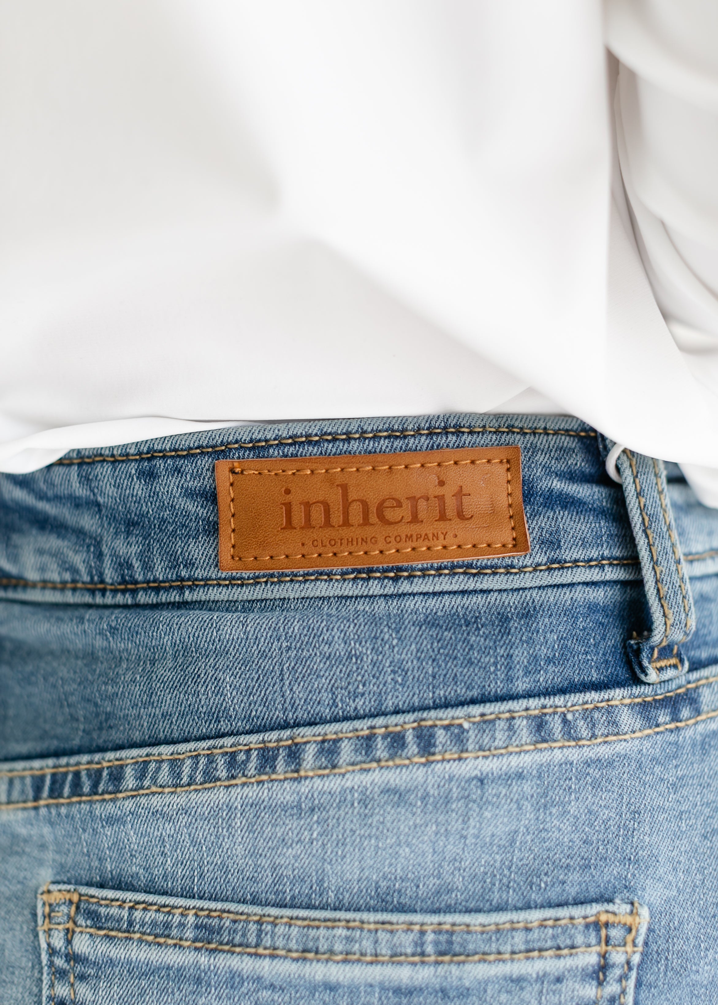 Close-up of blue jeans with 'inherit' brand label on a white background