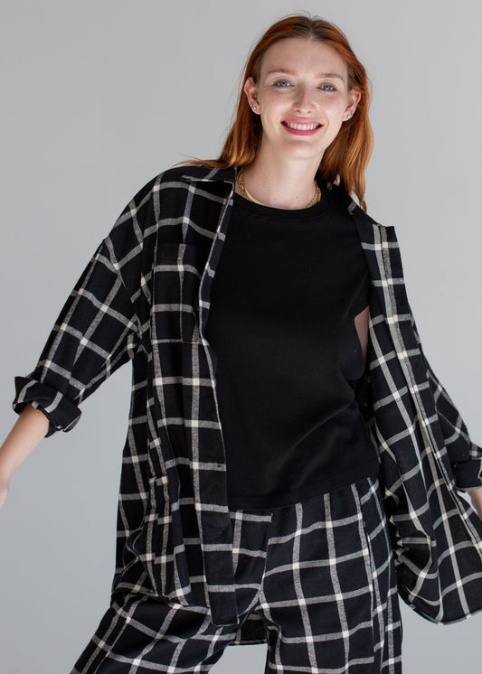 Woman wearing a black and white checkered shirt over a black top on a gray background
