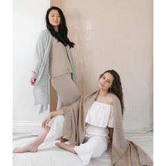 Two women wearing matching beige and white outfits against a neutral background