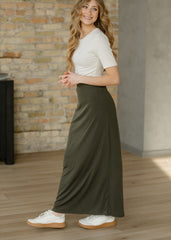 Woman wearing a white t-shirt and green skirt standing in a room with a brick wall.