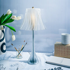 Decorative table lamp with a white shade on a surface with a vase, notebook, and other items.