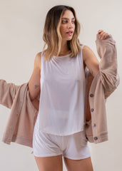 Woman wearing a white tank top and shorts with a beige jacket on a plain background