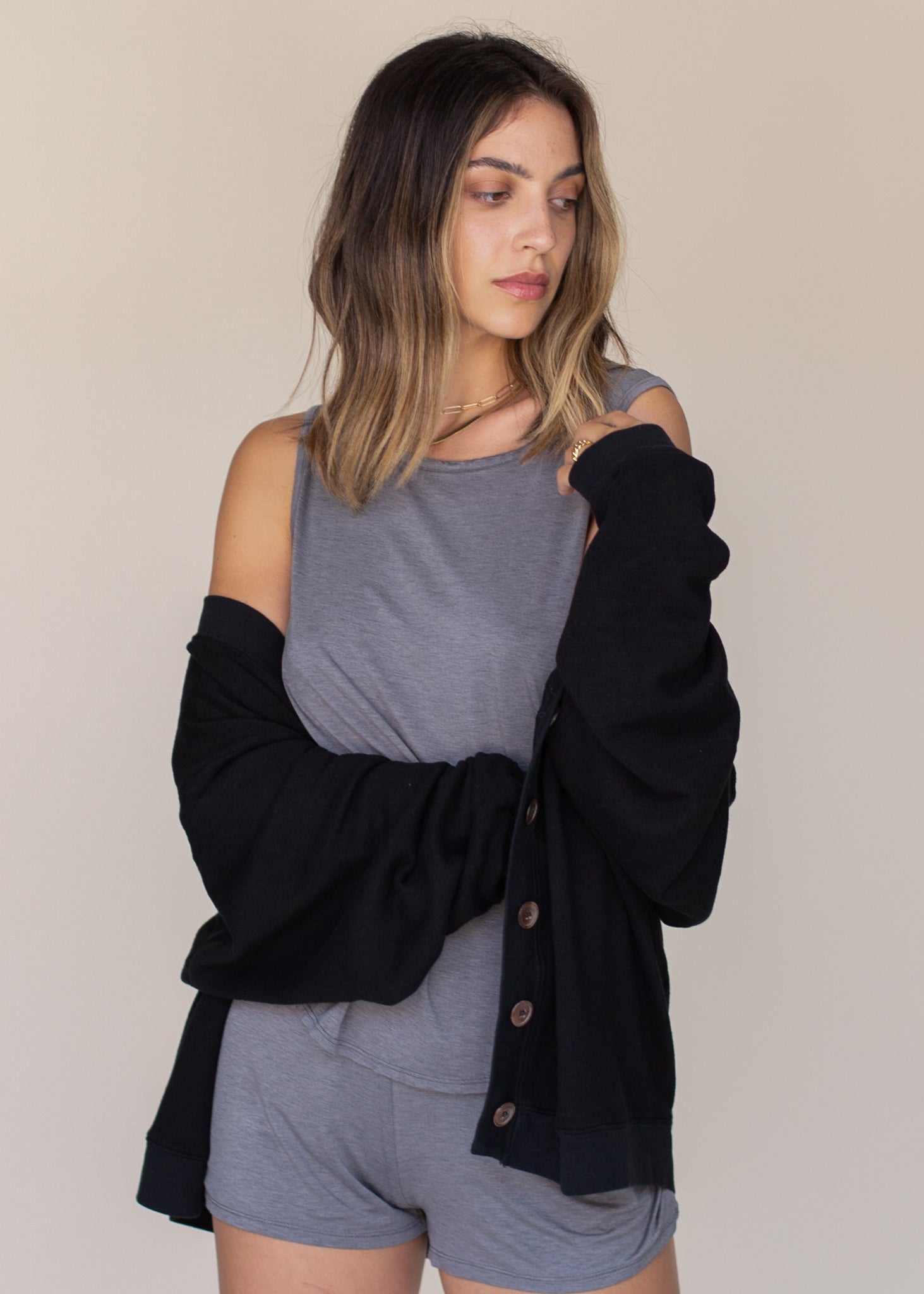 Woman wearing a black cardigan over a gray top and shorts on a beige background