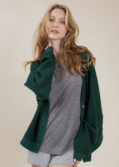 Woman wearing a green cardigan over a gray shirt and shorts on a beige background