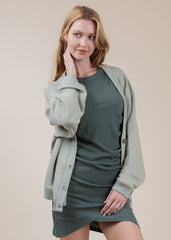 Woman wearing a green dress with a matching cardigan against a beige background