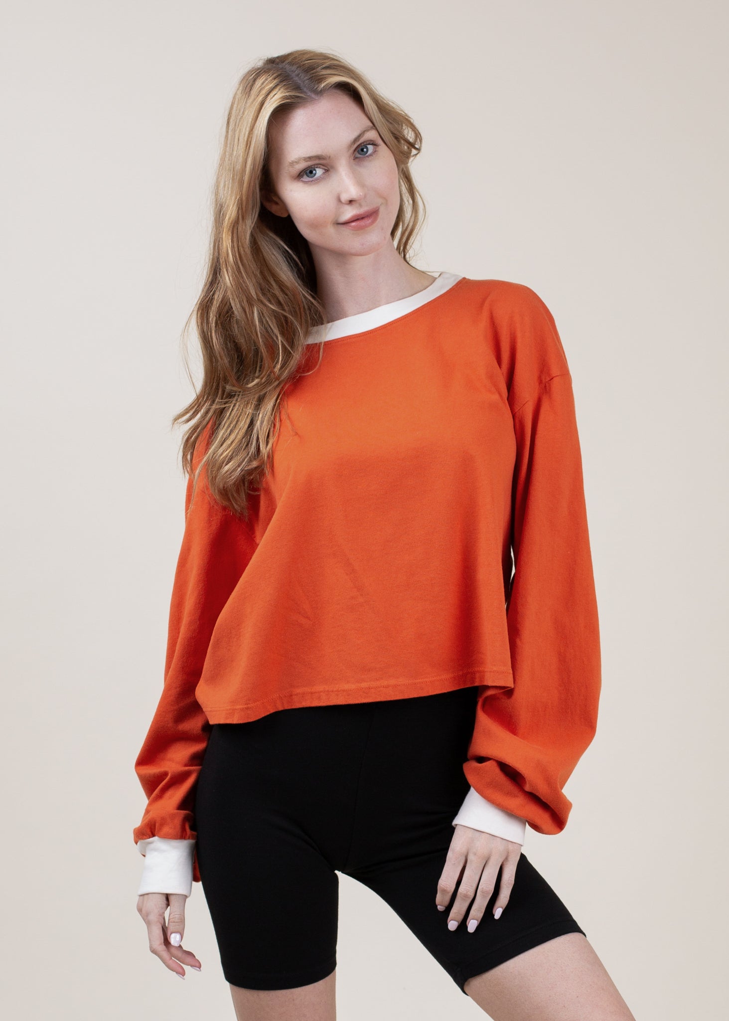 Woman wearing an orange sweatshirt and black shorts on a beige background