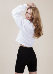 Woman wearing a white long-sleeve top and black shorts on a beige background