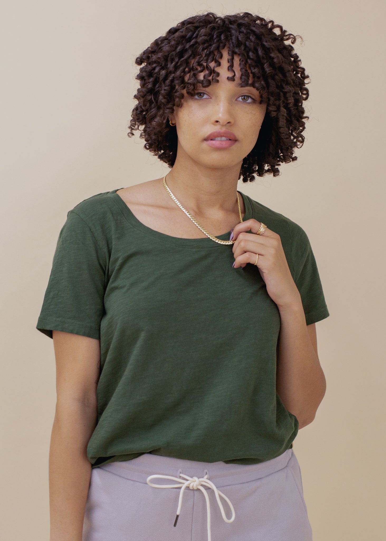 Woman wearing a green t-shirt and light purple pants against a beige background
