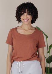 Person wearing a brown t-shirt and gray pants with a plant in the background