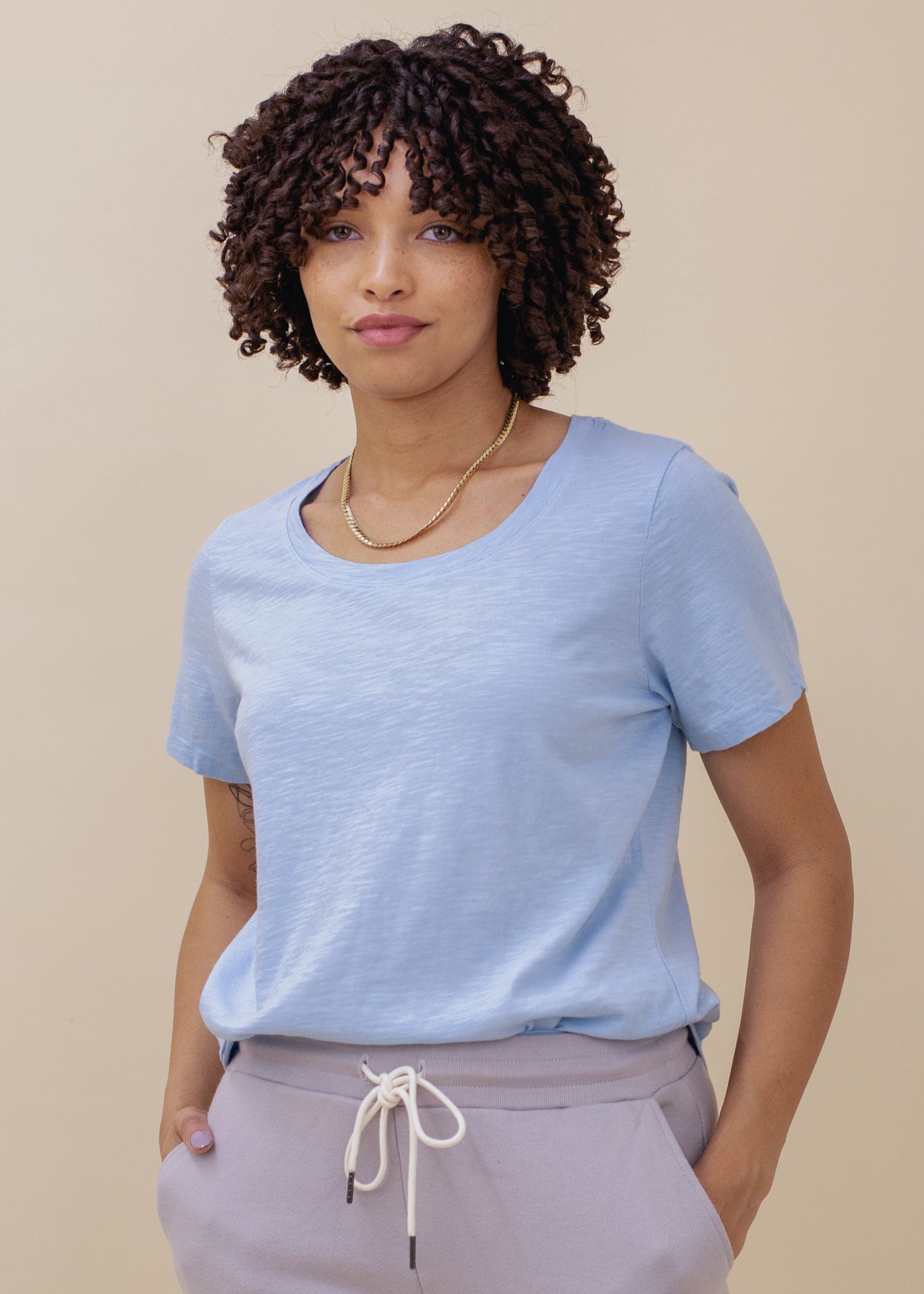 Woman wearing a light blue shirt and gray pants against a beige background