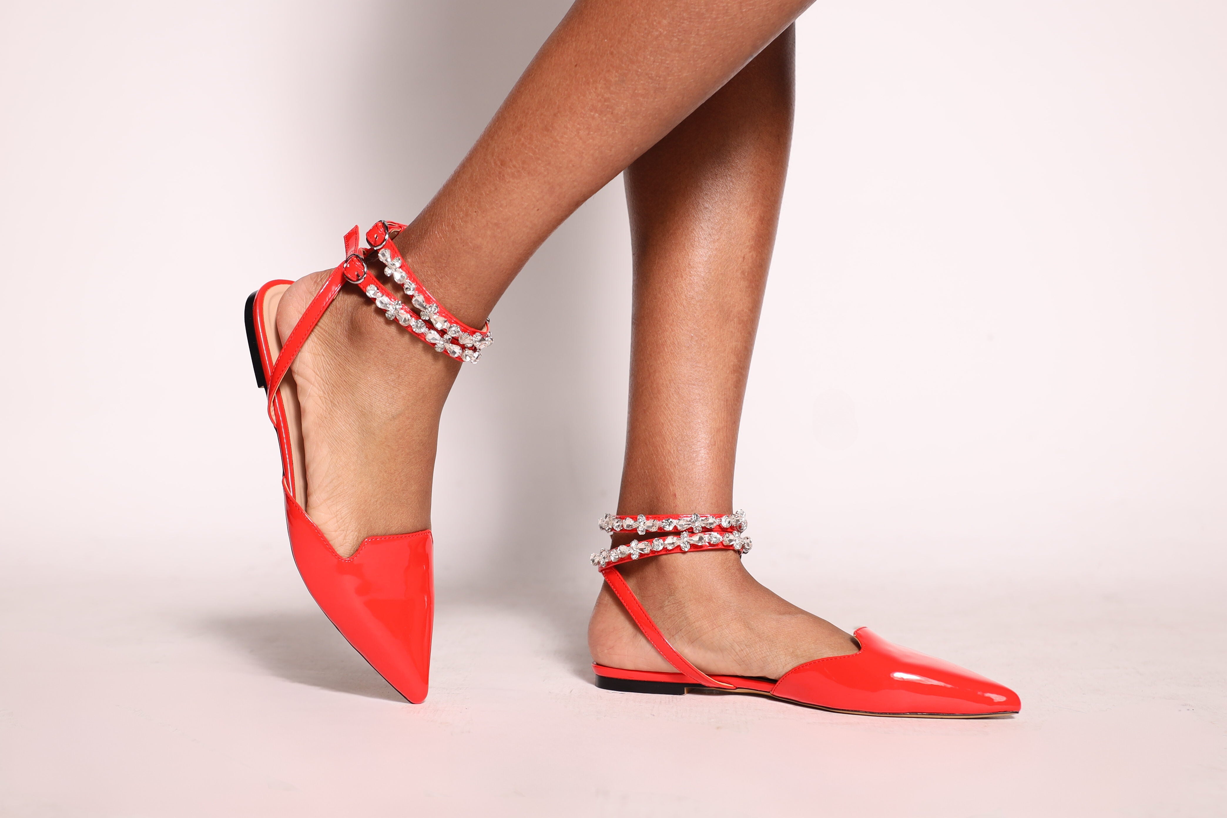 Red pointed-toe flats with ankle straps on a light background