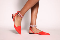 Red pointed-toe flats with ankle straps on a light background