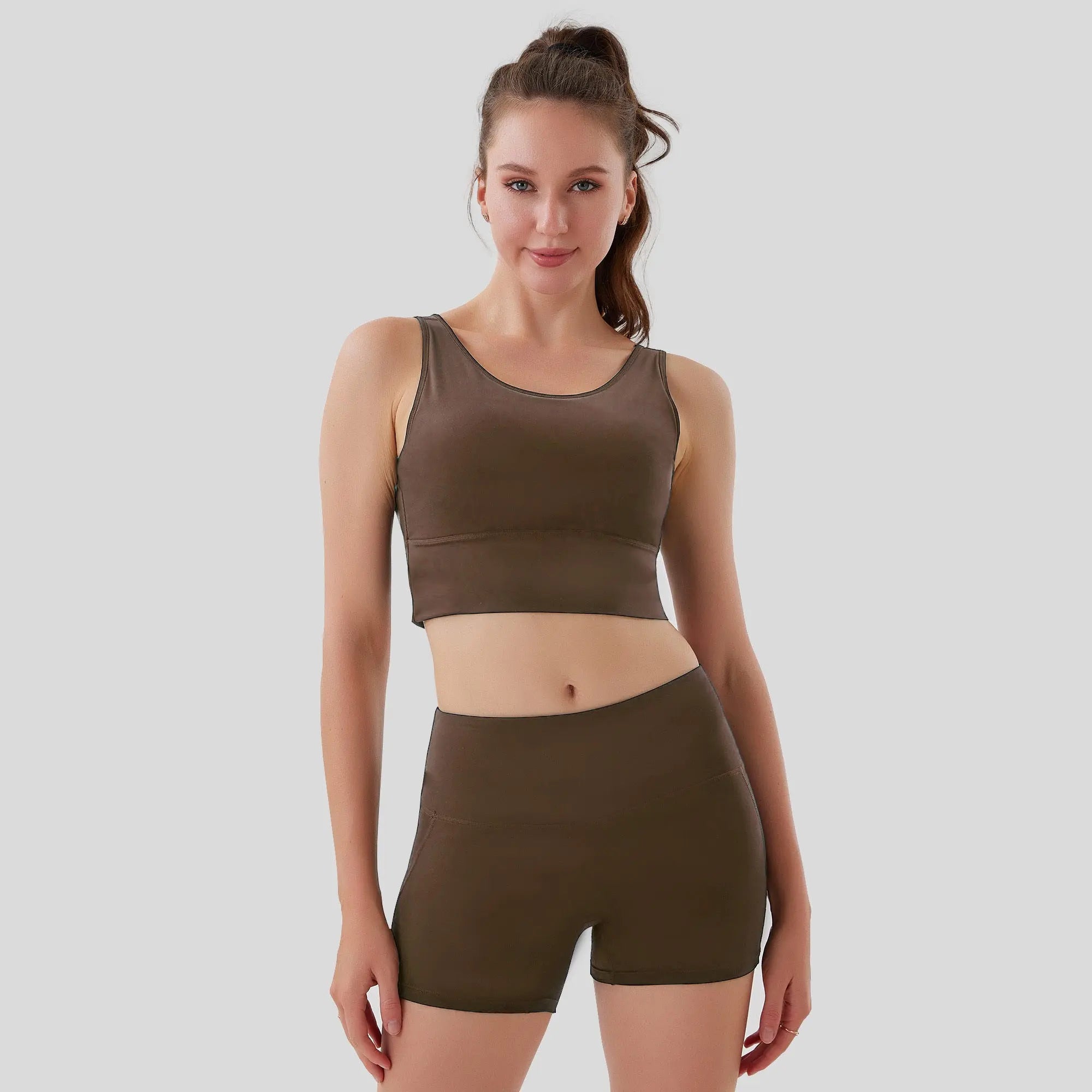 Woman wearing a brown sports bra and shorts set on a light gray background