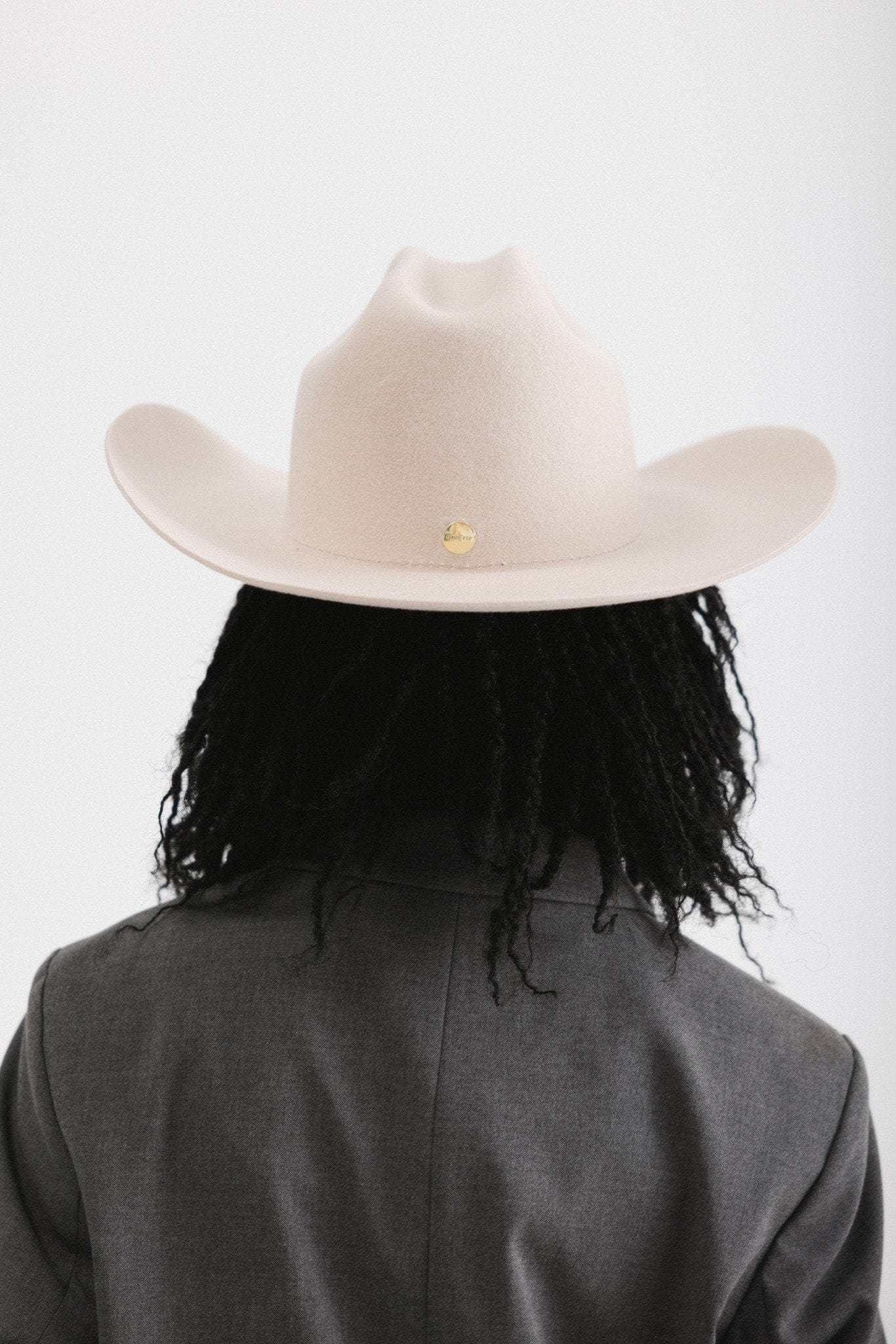 Person wearing a beige cowboy hat and dark coat on a white background