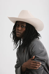 Person wearing a beige cowboy hat and gray coat on a white background